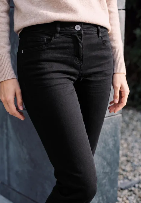 Enge schwarze Jeans und beige Pullover, Nahaufnahme von Taille und Beinen.