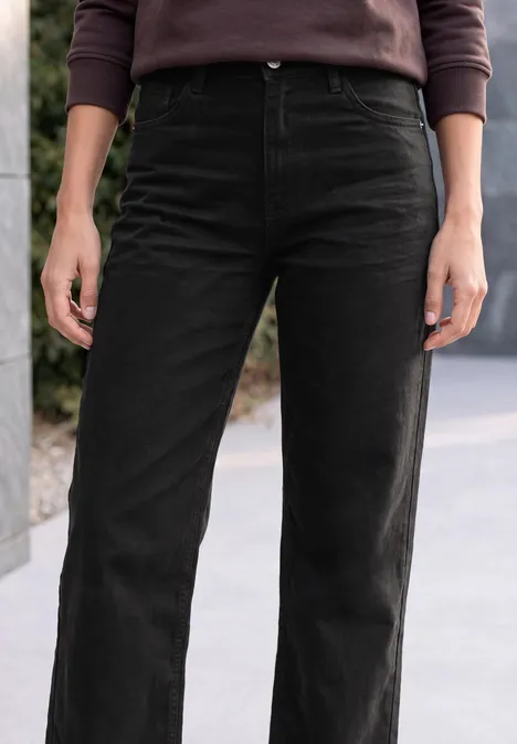 High Waist Wide Leg Jeans im Loose Fit Black Frau trägt eine schwarze, gerade geschnittene Hose und einen dunklen Pullover, steht draußen.