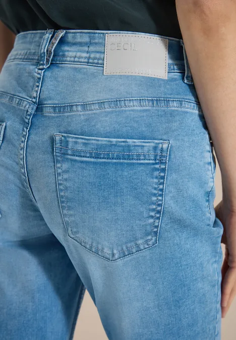 Jean taille moyenne, coupe Slim Leg et style décontracté light blue wash Femme de dos portant un jean bleu clair avec poche arrière et étiquette blanche, haut noir.