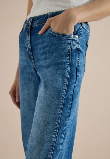 Jean à jambes larges avec des bandes en galon mid blue wash Une personne porte un jean bleu et un débardeur blanc, main dans la poche.