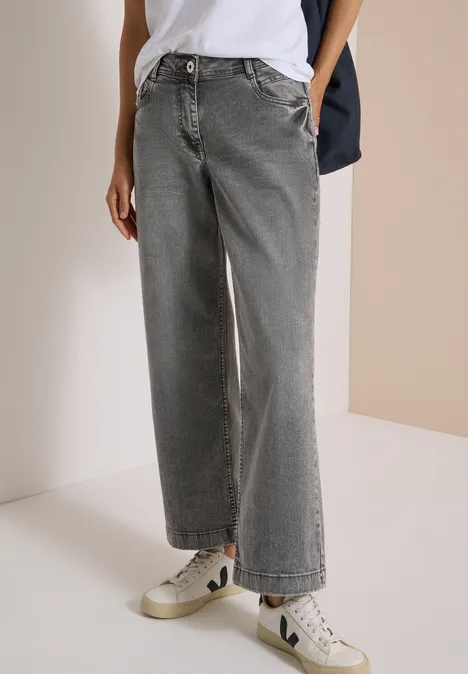 Ein Model trägt weite, graue High-Waist-Jeans und weiße Sneaker.