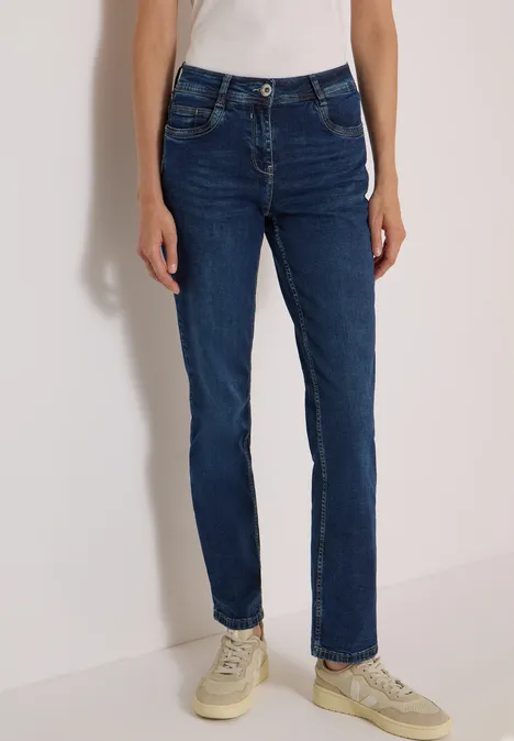 Eine Person trägt dunkelblaue Slim-Straight-Jeans mit hellen Sneakern.