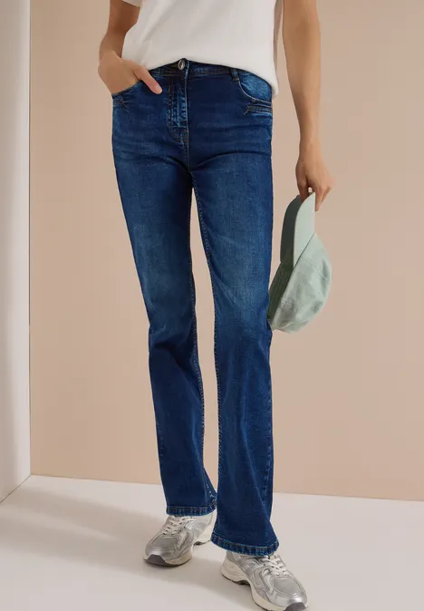 High Waist Bootcut Jeans im Slim Fit mid blue used wash Person trägt blaue Jeans, weißen Oberteil und Sneaker, hält eine Schirmmütze in der Hand.