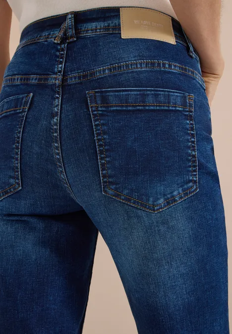 High Waist Bootcut Jeans im Slim Fit mid blue used wash Rückenansicht einer Person in dunklen Jeans mit ausgeprägten Gesäßtaschen.