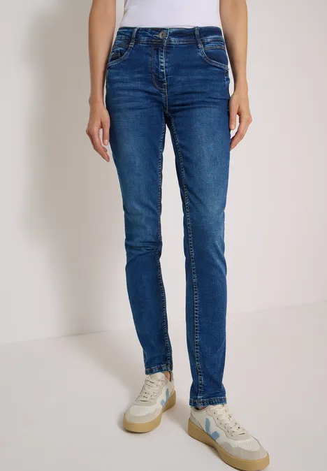Person trägt enge blaue Jeans und weiße Sneaker.