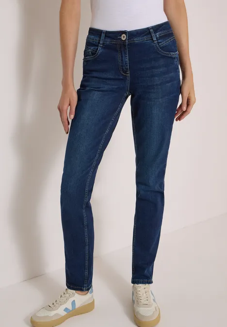 Person trägt dunkelblaue Skinny-Jeans und helle Sneaker vor neutralem Hintergrund.