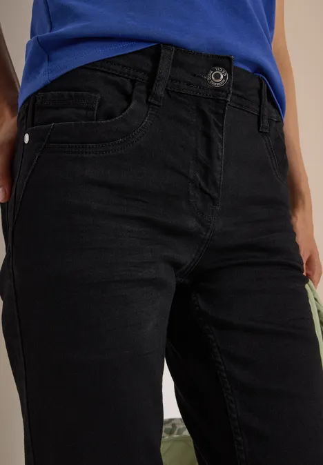 Eine Person trägt schwarze Jeans und ein blaues Oberteil, Nahaufnahme des Hüft- und Beinbereichs.