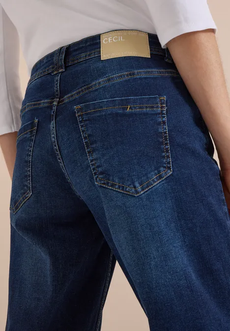 Rückansicht einer Person in blauen Jeans mit dezentem Label und weißem Oberteil.