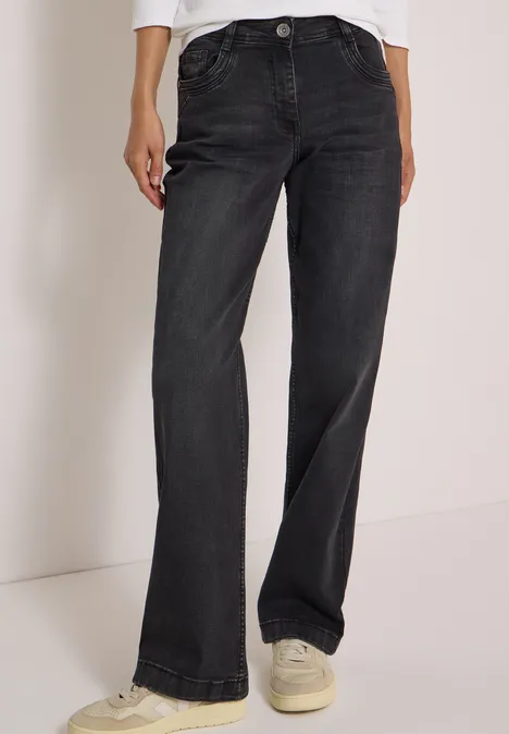 Schwarze, gerade geschnittene Jeans mit weißen Sneakern an einem stehenden Modell.