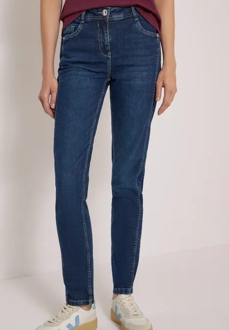 Personne en jean skinny bleu foncé et baskets blanches, seules les jambes et les pieds sont visibles.