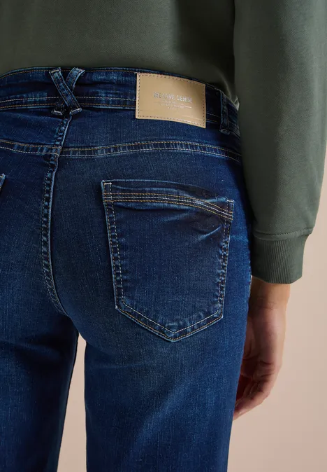 Eine Person trägt dunkle Jeans und ein grünes Sweatshirt, Ansicht von hinten.