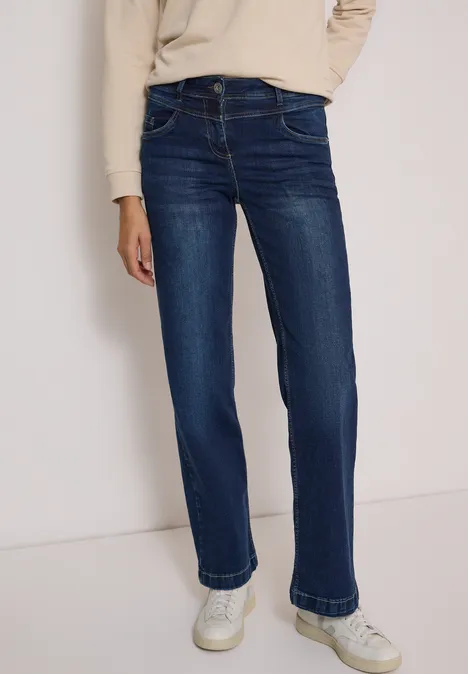 Eine Person trägt dunkelblaue, gerade geschnittene Jeans und weiße Sneaker.