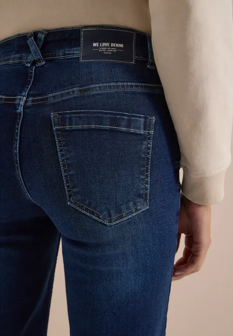 Rückansicht einer dunklen Jeanshose mit aufgesetzten Taschen und Markenlabel am Bund, getragen von einer Person.