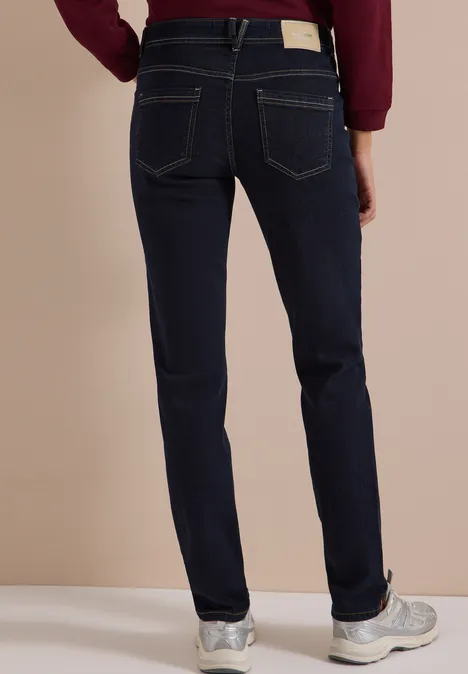 Rückenansicht einer Person in dunkelblauen Jeans und weißen Sneakern.