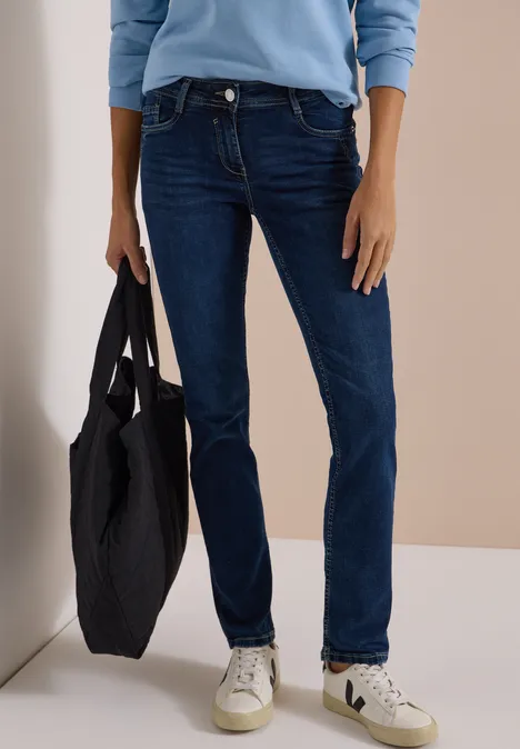 Person in dunklen Jeans, weißen Sneakers und hellblauem Oberteil trägt eine schwarze Tasche.