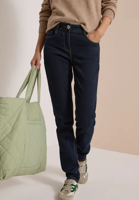 High Waist Slim Leg Jeans Slim Fit rinsed wash Person in dunklen Jeans, beigem Pullover und Sneakern hält eine große, hellgrüne Tasche.