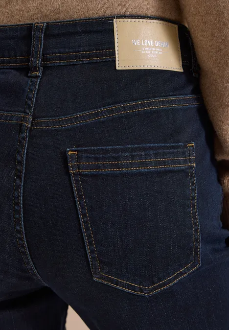 High Waist Slim Leg Jeans Slim Fit rinsed wash Rückenansicht in dunkler Jeans mit Gesäßtasche, beigefarbenem Label und braunem Mantel.