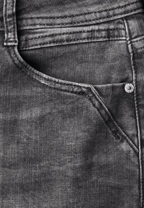 Close-up van een donkerblauwe spijkerbroek met achterzak, stiksels en een klinknagel.