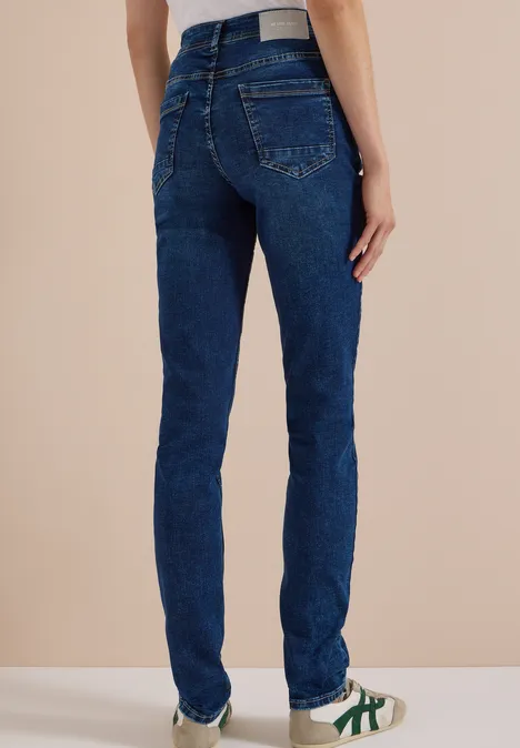 Nahaufnahme von einer Person von hinten in dunkelblauen Jeans und weißen Sneakers mit grünen Streifen.