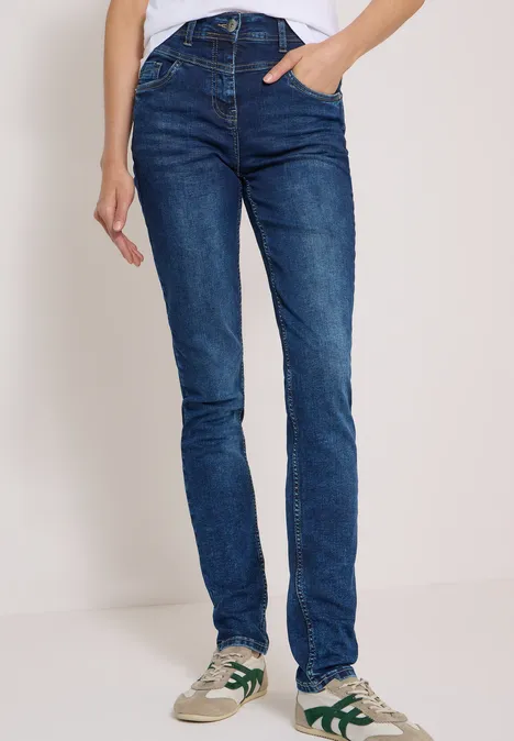 Person trägt schmale blaue Jeans und weiße Sneakers mit grünen Details.
