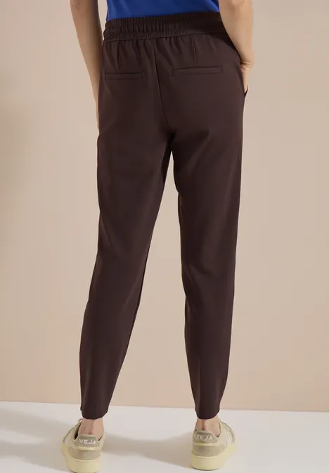 Bruine broek met hoge taille, elastische tailleband en taps toelopende pijpen, van achteren gezien.