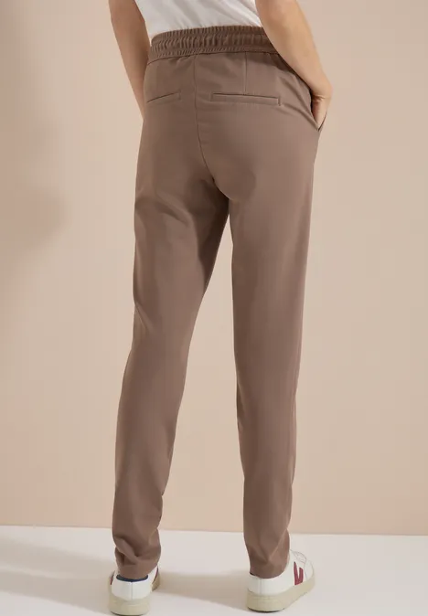 Mid Waist Slim Leg Hose im Casual Fit earthy taupe Rückansicht einer Person in beigen Jogginghosen und weißen Sneakers vor neutralem Hintergrund.