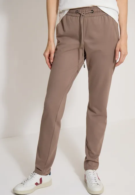 Mid Waist Slim Leg Hose im Casual Fit earthy taupe Locker sitzende hellbraune Jogginghose mit Kordelzug und weißen Sneakern.