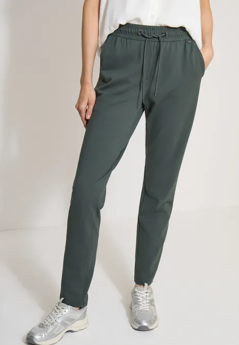 Model draagt een donkergroene casual broek met trekkoord en zilverkleurige sneakers.