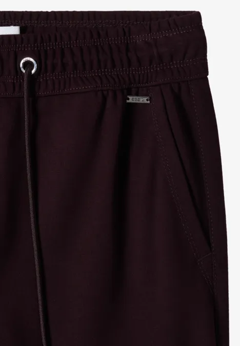Gros plan sur un pantalon de jogging bordeaux avec ceinture élastique, cordon de serrage et poche latérale.