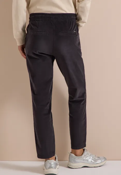 Vue de dos d'une personne portant un pantalon foncé et des baskets argentées sur fond neutre.