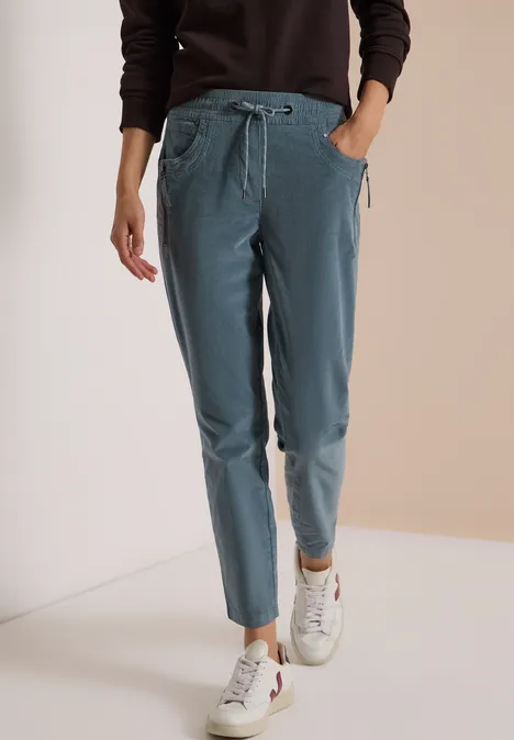 Pantalon de jogging femme bleu clair à taille élastique et poches, porté avec baskets blanches.