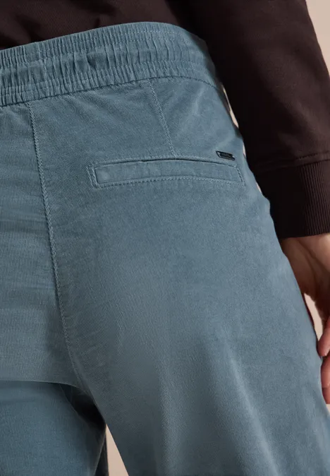 Vue arrière d'une personne en pantalon velours côtelé bleu clair et haut noir, focus sur la poche