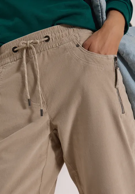 Gros plan d’une personne portant un pantalon beige à cordon et poches, main dans la poche.