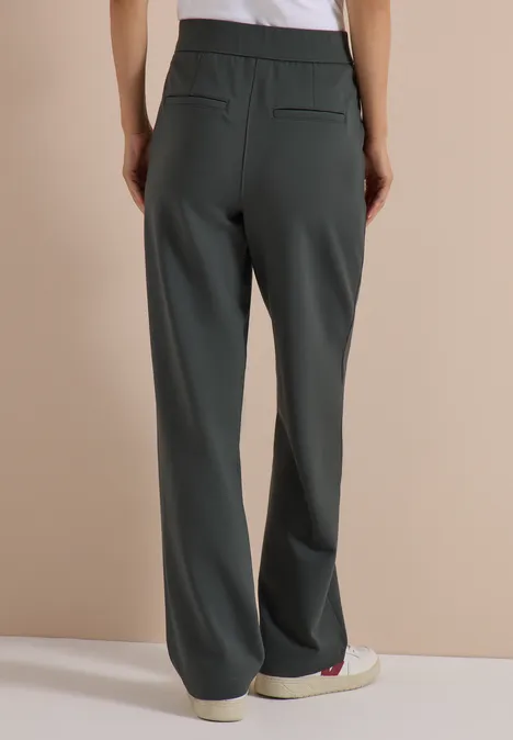 Femme portant un pantalon droit et ample gris foncé, vue de dos dans un style minimaliste.