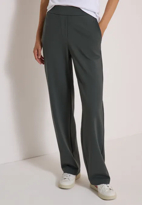 Pantalon femme ample vert foncé à coupe droite, poches latérales, porté avec des baskets blanches.