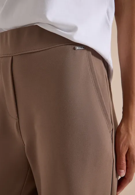 Gros plan sur une personne portant un pantalon marron et un haut blanc, main près de la poche.