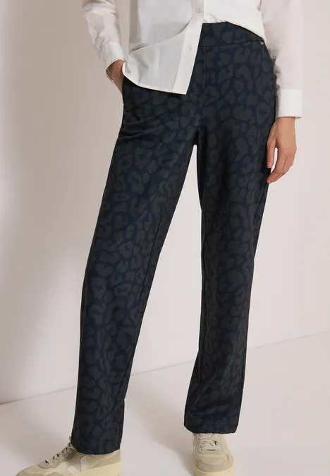 Dunkelblaue, gerade geschnittene Hose mit dezentem Muster, kombiniert mit weißer Bluse und hellen Sneakern.