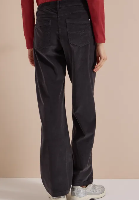 Vue de dos d'une personne en pantalon large noir en velours côtelé et baskets sur fond beige.