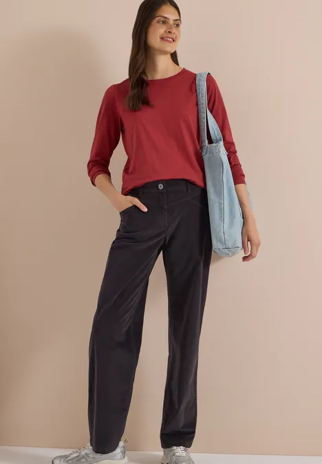 Femme portant un pull rouge, un pantalon noir ample et un sac en tissu sur un fond beige.