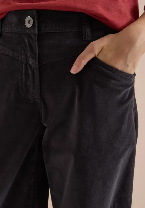 Gros plan d'une personne en haut rouge et pantalon en velours côtelé sombre, main dans la poche.