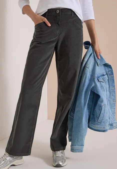 Personne porte un pantalon noir large avec poches, un haut blanc, baskets argentées et tient une veste en jean claire.