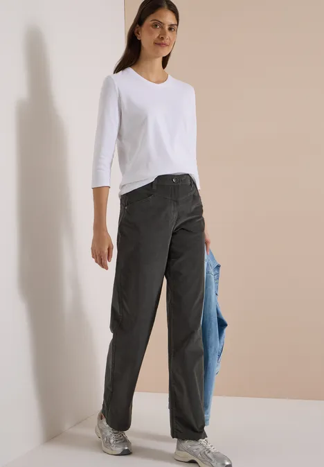 Femme en t-shirt blanc 3/4, jeans noirs et baskets, tenant une veste bleu clair décontractée à la main.