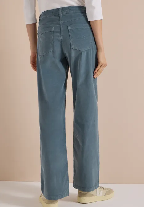 Vue arrière d'une personne portant un pantalon large en velours côtelé bleu et des baskets claires.