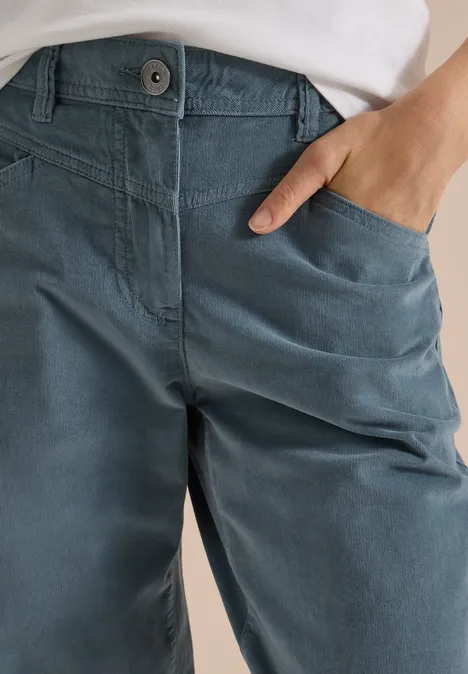 Gros plan sur un pantalon bleu en coton, main dans la poche et bord supérieur blanc visible.