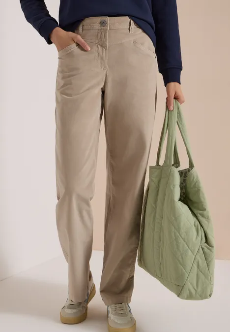 Vue de la partie basse du corps, pantalon beige ample, baskets vert pâle et sac matelassé vert.