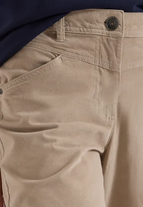 Gros plan sur un pantalon beige clair en velours côtelé avec poches latérales et bouton apparent.