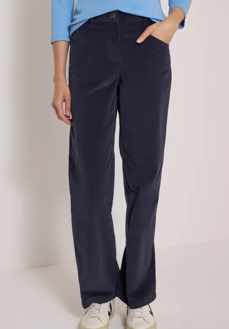 Personne en pantalon velours côtelé bleu foncé, t-shirt bleu clair et baskets blanches sur fond neutre.