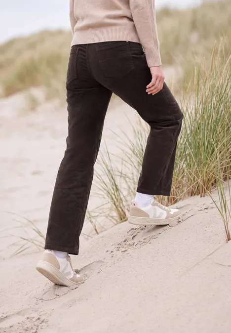 Person in schwarzer Hose und hellen Schuhen erklimmt eine Düne mit Strandgras.