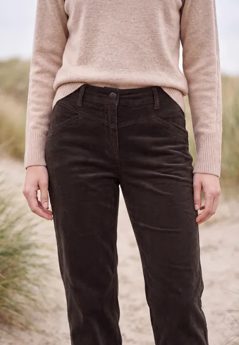 Person steht vor Dünengras am Strand, trägt einen beigen Pullover und schwarze Cordhose