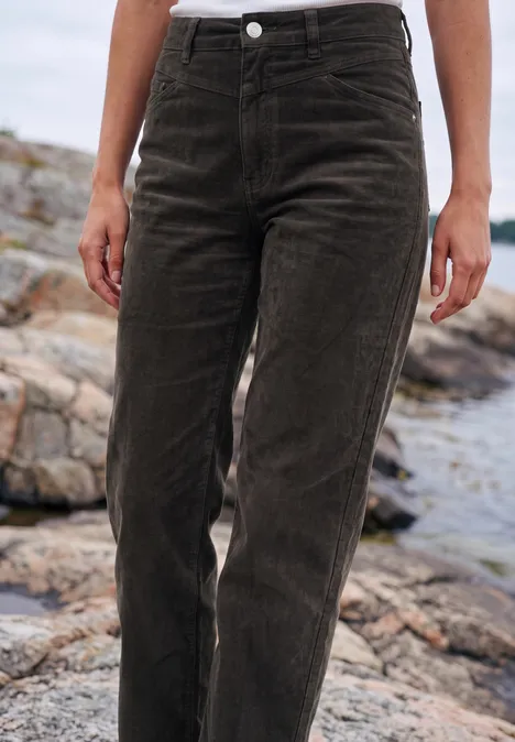 Eine Person steht auf Felsen und trägt eine dunkelbraune Cordhose.
